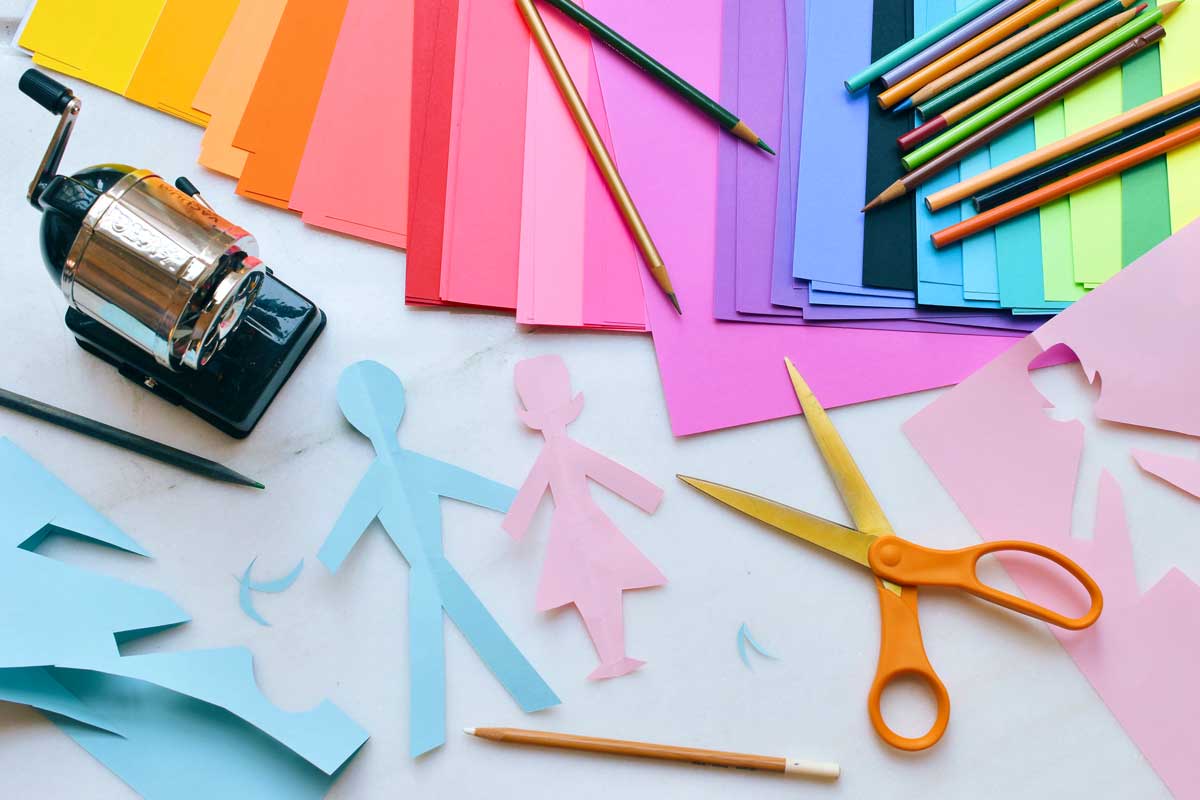 Buntes Papier, Schere, Bleistift und Anspitzer auf Tisch