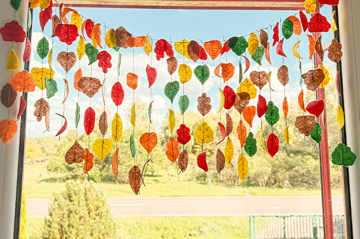 Ganz viele bunte Herbstblätter aus Filz hängen an einer Girlande vorm Fenster