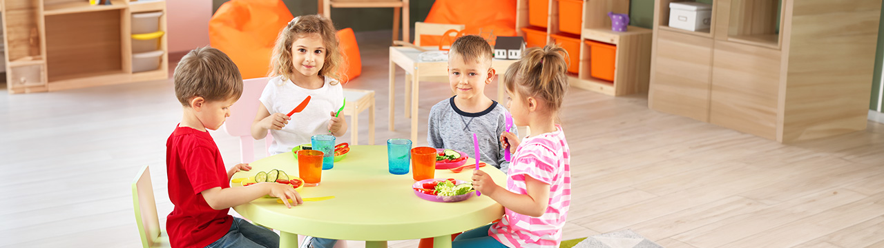 Möbel & Raumausstattung Kitakinder sitzen am Tisch und essen im Kindergarten einen Salat