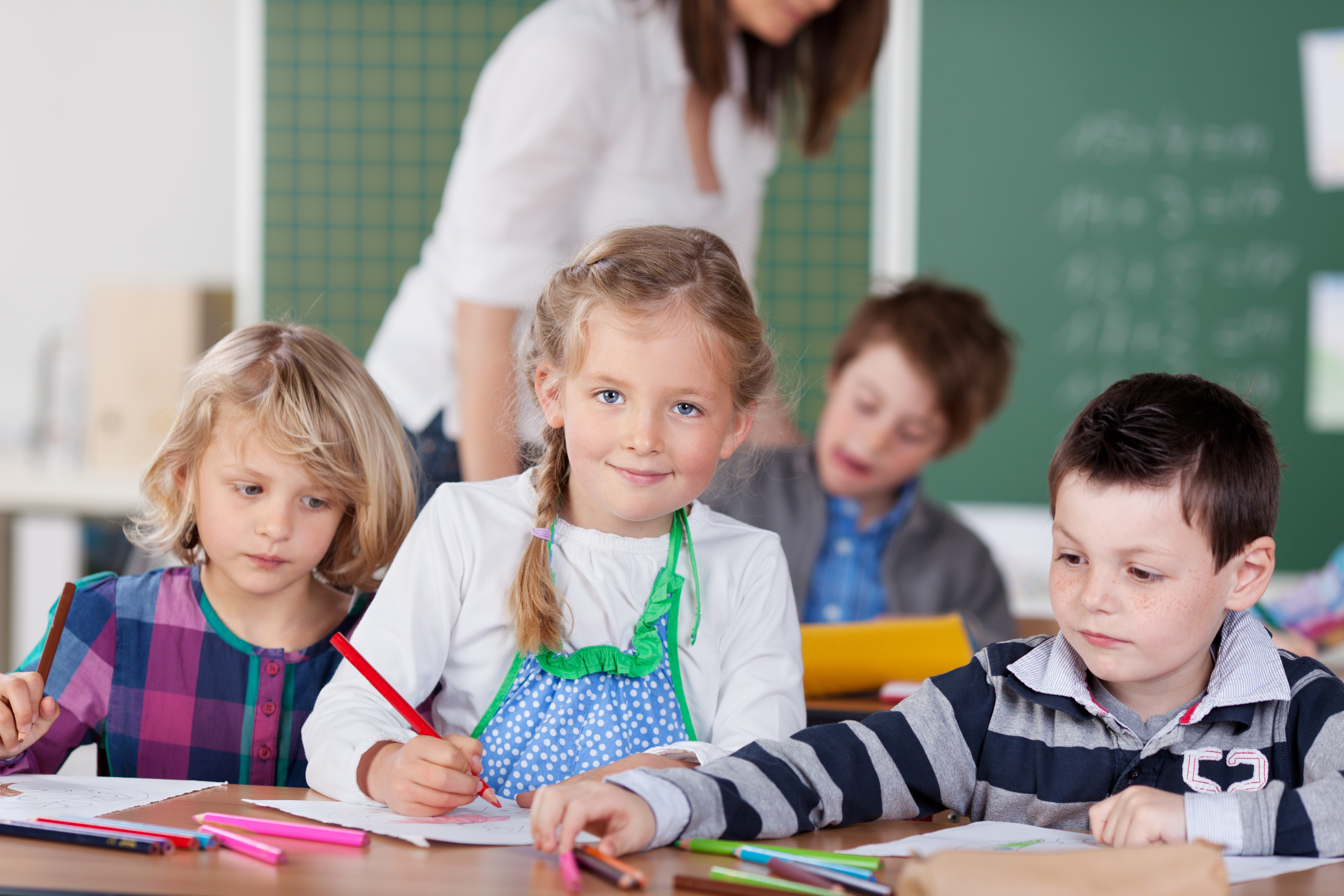 Schülerin mit Stift in der Hand sitzt am Tisch im Klassenraum
