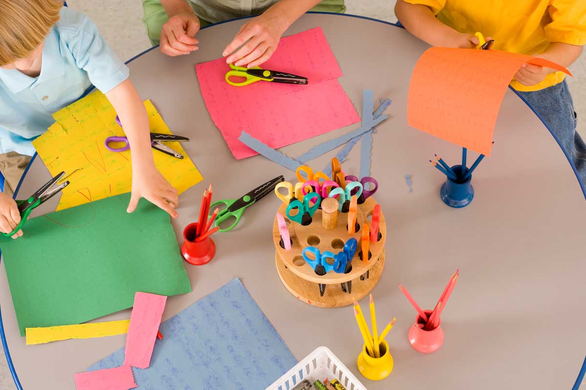 Kinder sitzen an eine Tisch und schneiden buntes Tonpapier aus