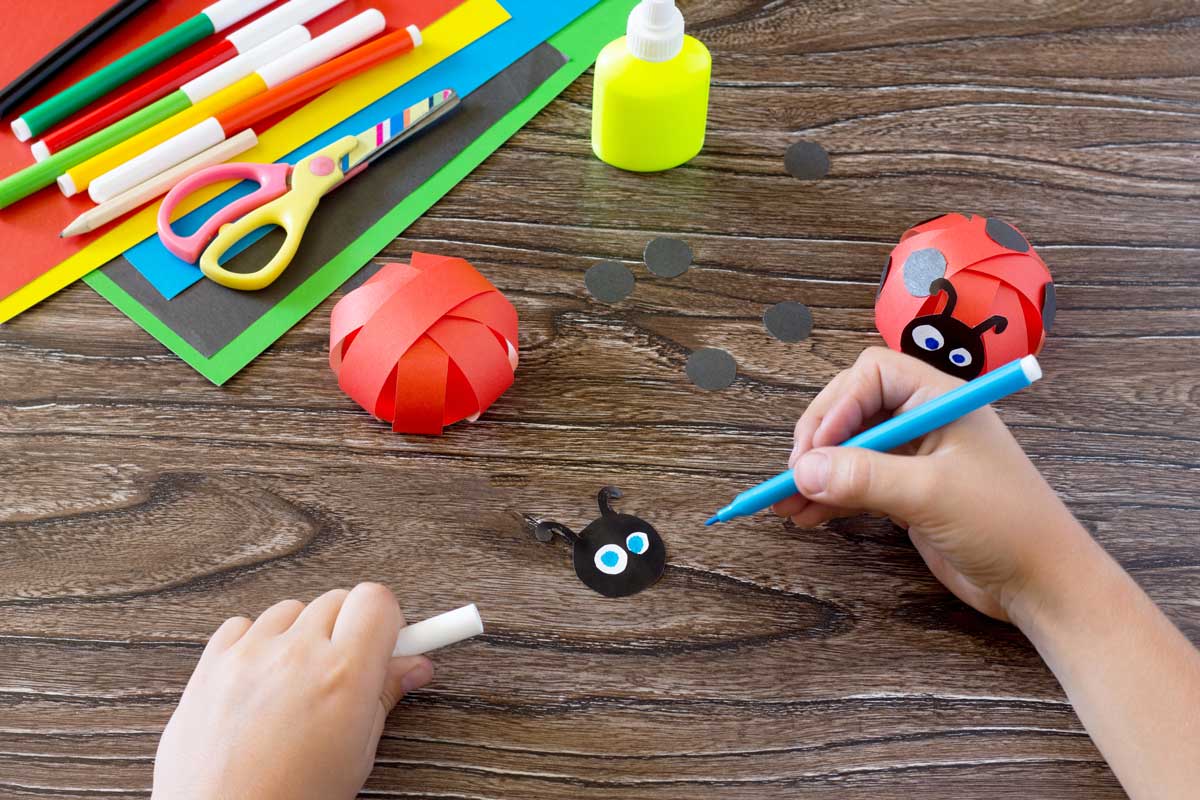 Kind bastelt einen Marienkaefer aus Papier