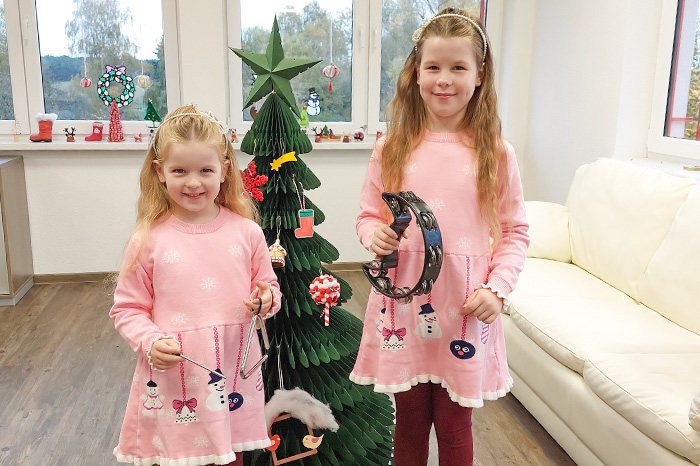Weihnachtslieder Mädchen stehen mit Musikinstrumenten vorm Weihnachtsbaum