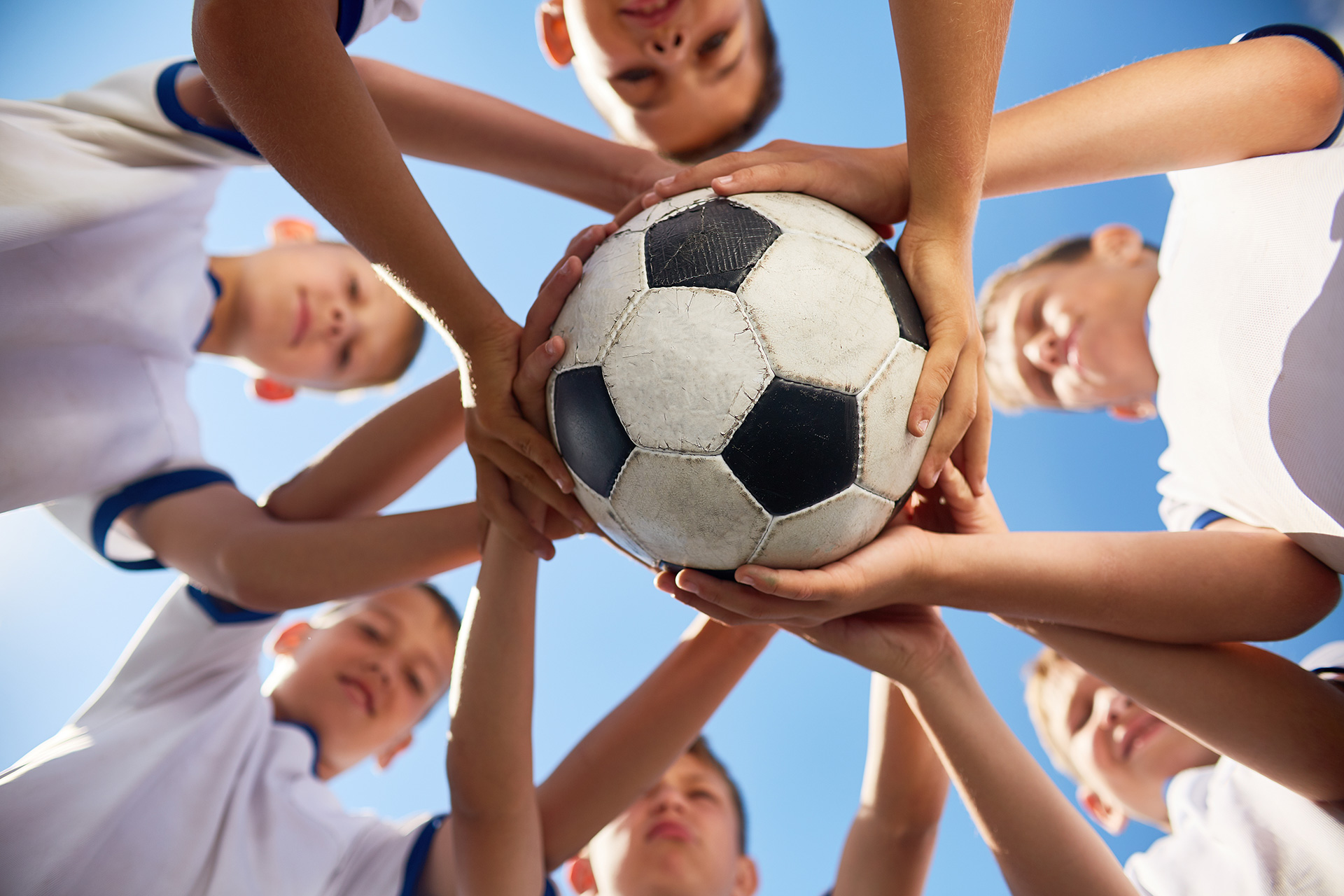 Kinder halten alle zusammen einen Fußball, Blick von unten