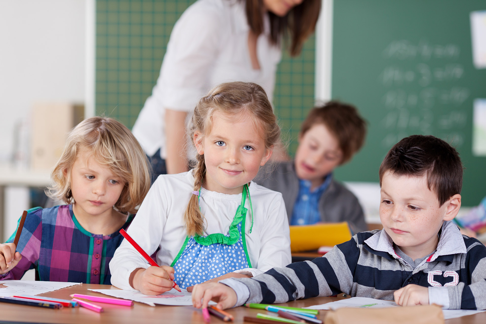 Schülerin mit Stift in der Hand sitzt am Tisch im Klassenraum