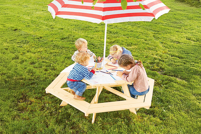 Vier Kinder sitzen an einem Outdoor-Picknicktisch mit Sonnenschirm und malen