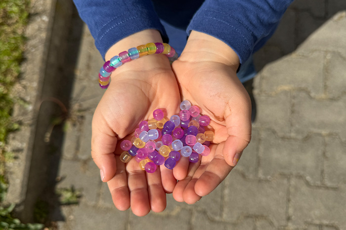 Kind hält lose UV-Perlen in den Händen und hat ein Armband mit UV-Perlen am Handgelenk